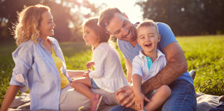 Eine verköpfige Familie sitzt auf einer Wiese und lacht gemeinsam.