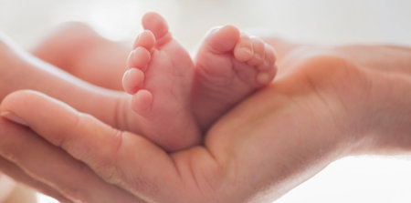 Die Füße eines Babys, die in der Hand einer erwachsenen Person liegen.