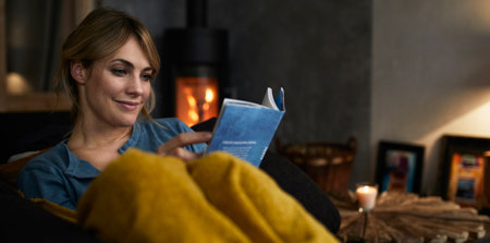 Eine Frau sitzt auf ihrem Sofa und ließt dabei ein blaues Buch.