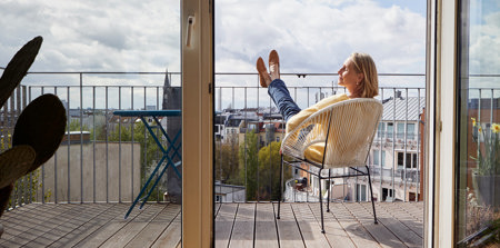 Eine Frau, die auf dem Balkon sitzt und mit geschlossenen Augen ihr Gesicht in Richtung der Sonne hält.